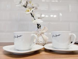 two white cups and saucers on a table with flowers at Casa de sub Nuc in Cluj-Napoca