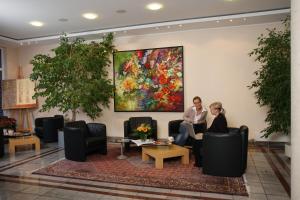 duas pessoas sentadas em cadeiras num átrio com um quadro em Stadthotel Oranienburg em Oranienburg