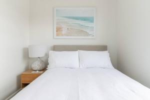 Una cama con sábanas blancas y una mesa con lámpara. en Sunset Sands on Esplanade By Host Solutions, en West Beach