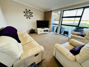 ein Wohnzimmer mit zwei Sofas und einem Flachbildfernseher in der Unterkunft Monarch Cottage on the Estuary in Athenree