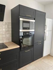 eine Küche mit schwarzen Schränken, einer Mikrowelle und einem Kühlschrank in der Unterkunft Ty Mamie spa - 700m de la plage in Saint-Pabu