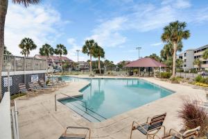 a swimming pool with chairs and palm trees at Mariners Cay 74 in Folly Beach
