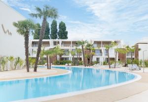 a large swimming pool with palm trees in front of a building at Casa Eolo Mare e Relax in Lido di Jesolo