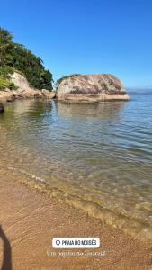 ein Strand mit einem großen Felsen im Wasser in der Unterkunft Apartamento em Enseada - Guarujá in Guarujá