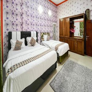two beds in a bedroom with purple wallpaper at Anaqi Homestay Mitra RedDoorz in Lahat