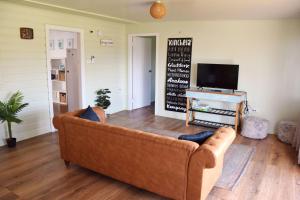a living room with a brown couch and a tv at Sea Salt Cottage - Bring your own linen. in South West Rocks