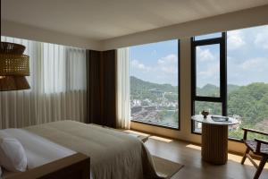 a hotel room with a bed and a large window at Yanyu Yunxi Resort Hotel 烟雨云兮酒店 in Fenghuang County