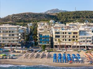 einen Strand mit blauen Sonnenschirmen, Stühlen und Gebäuden in der Unterkunft Steris Elegant Beach Hotel in Rethymno