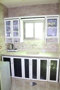una cucina con armadi bianchi, lavandino e due finestre di Rawan Residence Tyros 