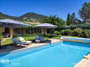 una piscina con sedie e ombrelloni accanto a una casa di GITE AUX 4 SAISONS DU COLORADO PROVENÇAL - 3 ÉTOILES - Rustrel a Rustrel