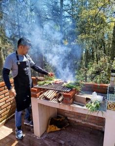 un hombre en un delantal cocinando comida en una parrilla en Finca de los Leones - Cabaña Primavera, en Pachuca de Soto