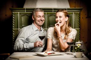 
a man and a woman sitting at a table with wine glasses at Sporthotel Ellmau in Tirol in Ellmau
