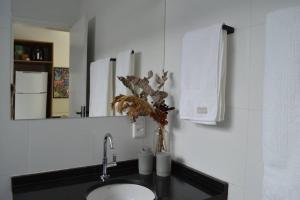a bathroom sink with a mirror and a vase with flowers at Kitnet equipada e aconchegante in Passos +15 photos