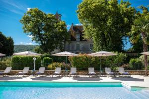 una piscina con sillas y sombrillas frente a una casa en Domaine de Monrecour - Hôtel & Restaurant - Proche de Sarlat, en Saint-Vincent-de-Cosse