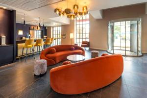 eine Lobby mit orangefarbenen Stühlen und einem Tisch und einer Bar in der Unterkunft Best Western Plus Hôtel Colbert in Châteauroux + 83 Fotos