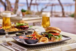 a plate with a sandwich and fries and two glasses of beer at Blue Sea Beach Resort in Faliraki