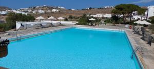 a large blue swimming pool with chairs and buildings at Traditional dream myconian studio in Ornos