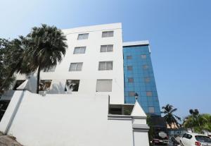 a white building with a palm tree in front of it at Super Townhouse Prince Palace in Trivandrum