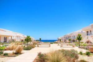 a walkway with benches in front of buildings and the ocean at Case del Sole Marzamemi Borgo 84 in Marzamemi