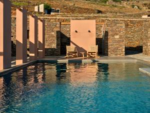 dwa krzesła siedzące obok basenu z wodą w obiekcie Under the Sun Cycladic Village w mieście Tinos