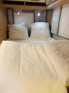a white bed with two pillows in an rv at 5 Sterne Wohnwagen all inclusive - direkt auf Messe Hannover - super beheizt - alles vor Ort - Wifi - Fully heated - Mobile Home all inclusive - at Fairground Hanover Trade Fair in Hannover