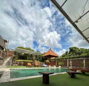 a swimming pool with two benches and an umbrella at Oka's Guest House Canggu in Canggu