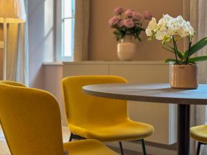 a table with yellow chairs and a vase of flowers at HOMEY I Teatro Romano Apartments in Trieste