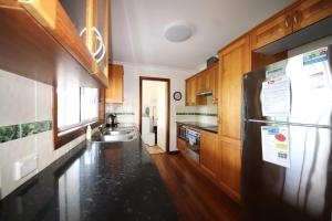 une cuisine avec des armoires en bois et un réfrigérateur noir dans l'établissement Kookaburra Cottage 71 Straight St HH, à Hat Head