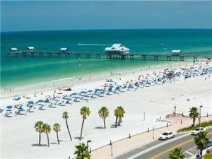 a beach with umbrellas and palm trees and a pier at Clearwater Beach Splendor - Weekly Beach Rental in Clearwater Beach