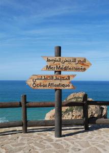 two wooden signs on a post next to the ocean at rare appartement de vacances in Tangier