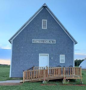 eine große blaue Scheune mit einer Tür und einer Holzveranda in der Unterkunft Old Schooling Summer Cottage in OʼLeary + 4 Fotos