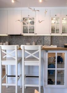 a kitchen with white cabinets and two white stools at WYSPA MEW - apartament PREMIUM z prywatnym ogrodem, 150 m od plaży in Gąski