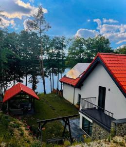 a white house with a red roof next to a lake at Stara Szafa - Komfortowy dom nad jeziorem in Łajs
