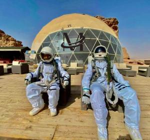 two astronauts in spacesuits sitting in front of a building at RUM MARTiN BUBBLES lUXURY CAMP in Wadi Rum