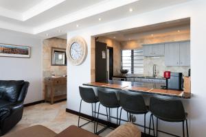 a kitchen with a bar with stools and a clock on the wall at Luxury Beachfront 706 with AC, Workspace & Table Mountain Views in Cape Town +23 photos