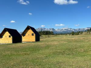 two houses in a field with mountains in the background at Eternum Glamping in Žabljak