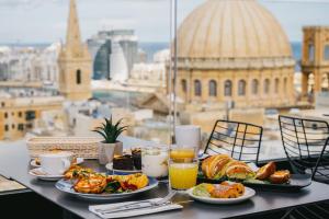 a table with plates of food and drinks and a view of the city at The Embassy Valletta Hotel in Valletta