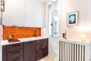 una cocina con armarios blancos y una pared de azulejos naranjas en GuestReady - Bright Apt near Sacré-Coeur, en París