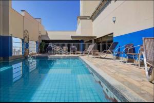a swimming pool with chairs and a table next to a building at Luix Londrina Flat Hotel , 707, QS completo in Londrina