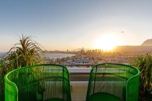two green chairs on a balcony with a view of a city at Hotel Madeira Centro in Benidorm