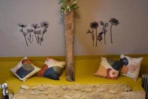 a yellow couch with pillows on it with flowers on the wall at Les Girouteaux La bergerie in Les Eyzies-de-Tayac