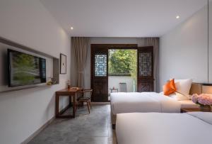 a bedroom with two beds and a table and a window at Mount Emei Heyuan Serene Residence Hot Spring Hotel in Emeishan City