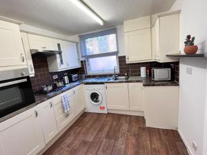 a kitchen with white cabinets and a washer and dryer at Abbey Wood Serviced Apartment 3BRH Free Wi-Fi Parking Tea and Coffee in Belvedere