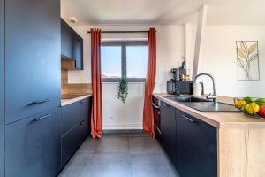 a kitchen with blue cabinets and a window with orange curtains at Le Saint-Jean - Hypercentre - Parking privé - 1 à 6 personnes - Wifi in Roubaix