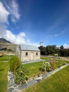 a barn with a garden and flowers in front of it at Historical Hicks Cottage in Queenstown