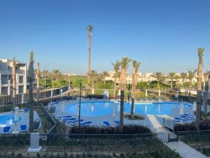 a resort with two pools with blue chairs and palm trees at Townhouse Villa Marassi North Coast in El Alamein