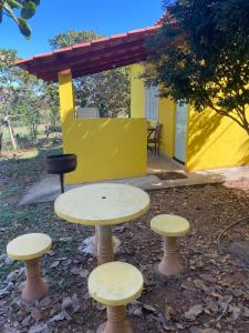 a table and four stools in front of a yellow building at Pousada Chalés Praia Vermelha in São João Batista do Glória
