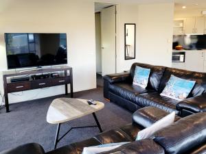a living room with leather couches and a tv at Hosts on the Coast Harbour View at Esplanade Apt 111 in Whitianga