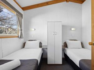 two beds in a small room with a window at Canberra Holiday Village in Canberra