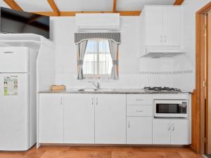 a white kitchen with white cabinets and a window at Canberra Holiday Village in Canberra +14 photos